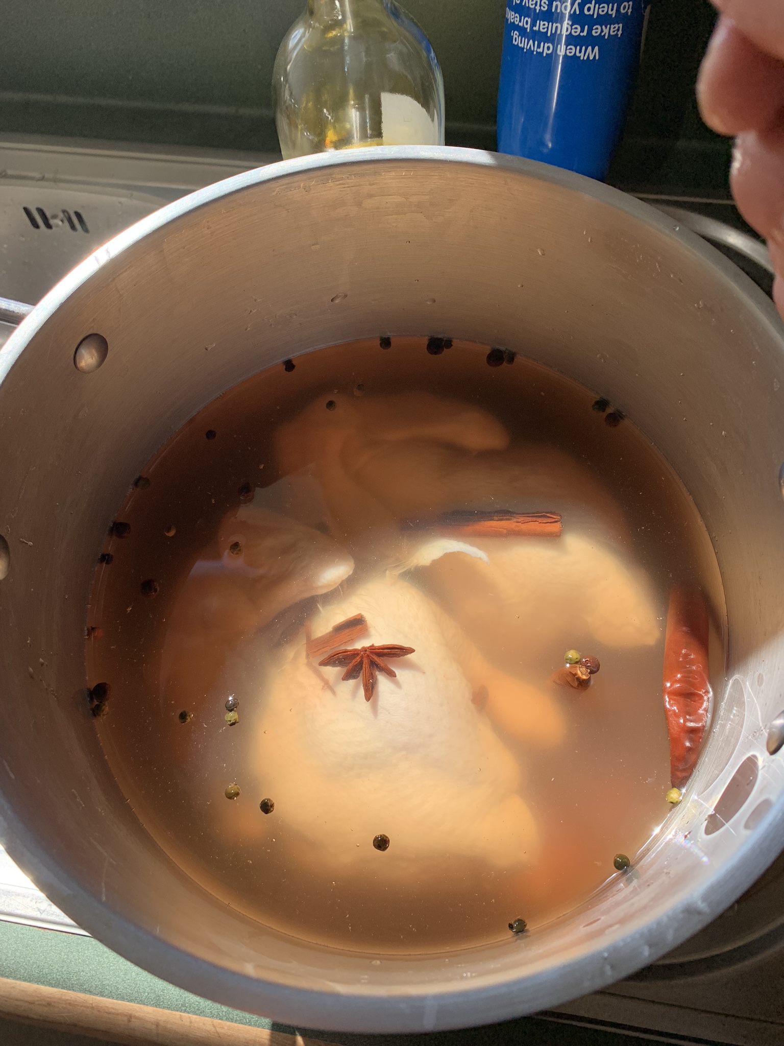 Two chickens in a pot, covered in brine. There are peppercorns, and cinnamon quills floating on top of the water. A star anise and a dried chilli drift languidly.