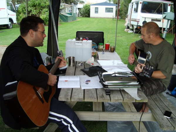 Eric and Russell, playing guitars at a picnic table while out camping