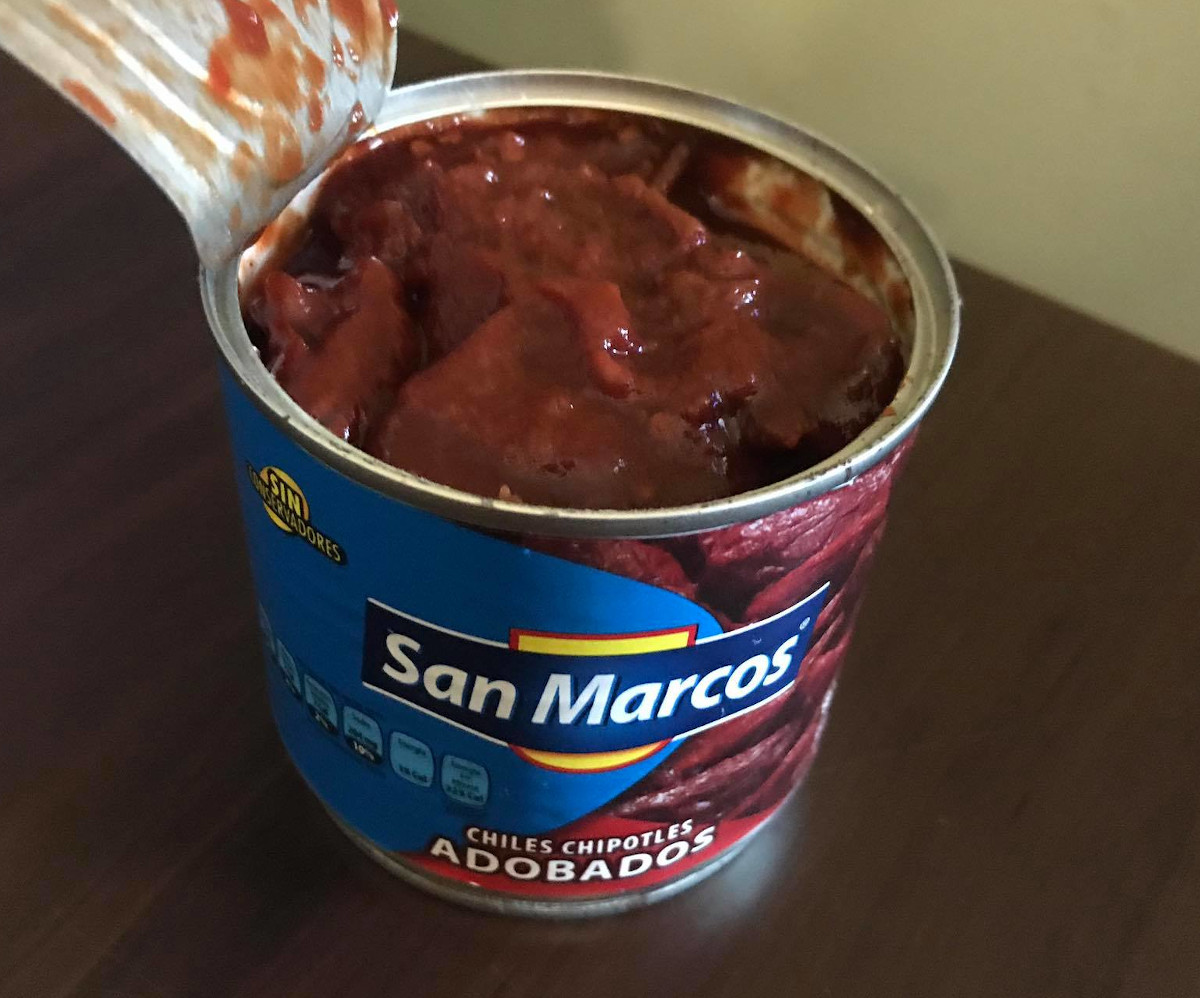 A can of chipotle peppers, opened to show them soaking in rich red-brown adobo sauce